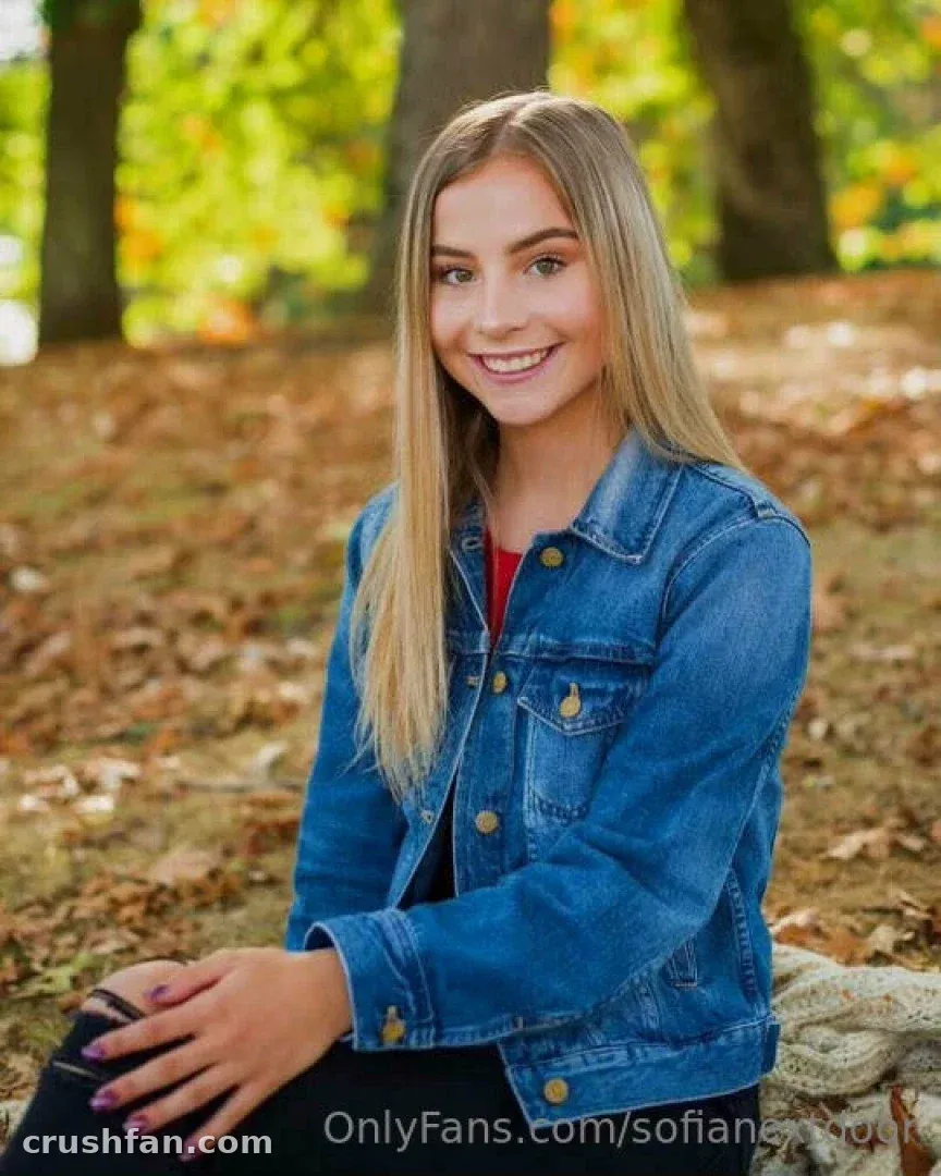 Sofianextdoor seated outdoors in a denim jacket among autumn leaves