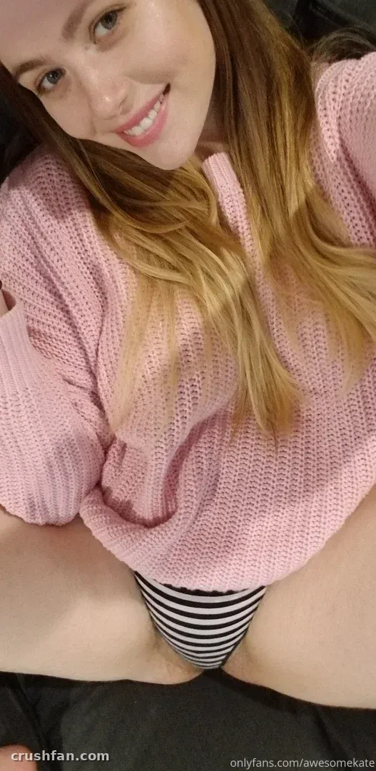 AwesomeKate lächelt in einem rosa Strickpullover und gestreiften Slips in einem nahen Selfie.