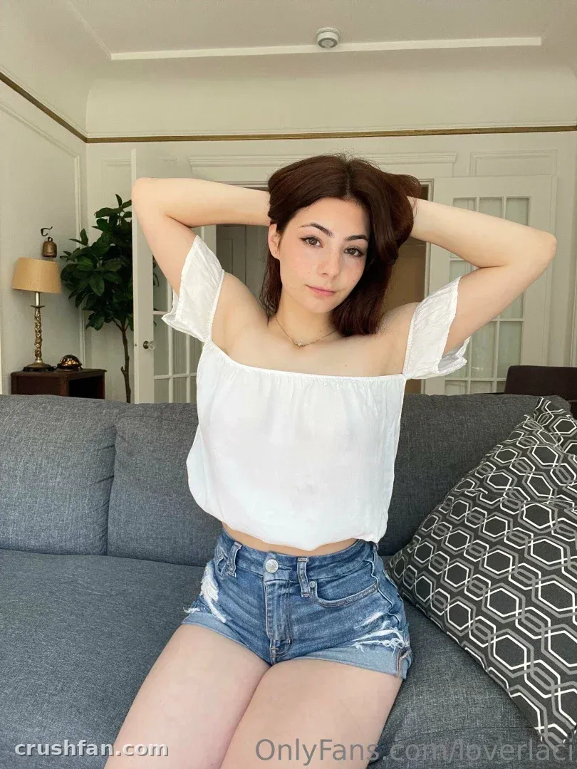 Laci Witton dans un haut blanc et un short en jean assise sur un canapé gris à l'intérieur