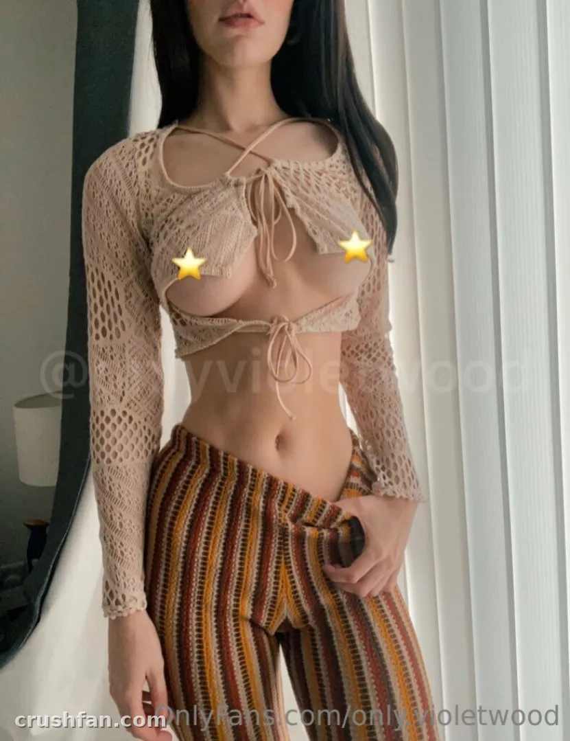 Criadora com um top cropped de crochê bege e calça listrada perto de uma janela iluminada