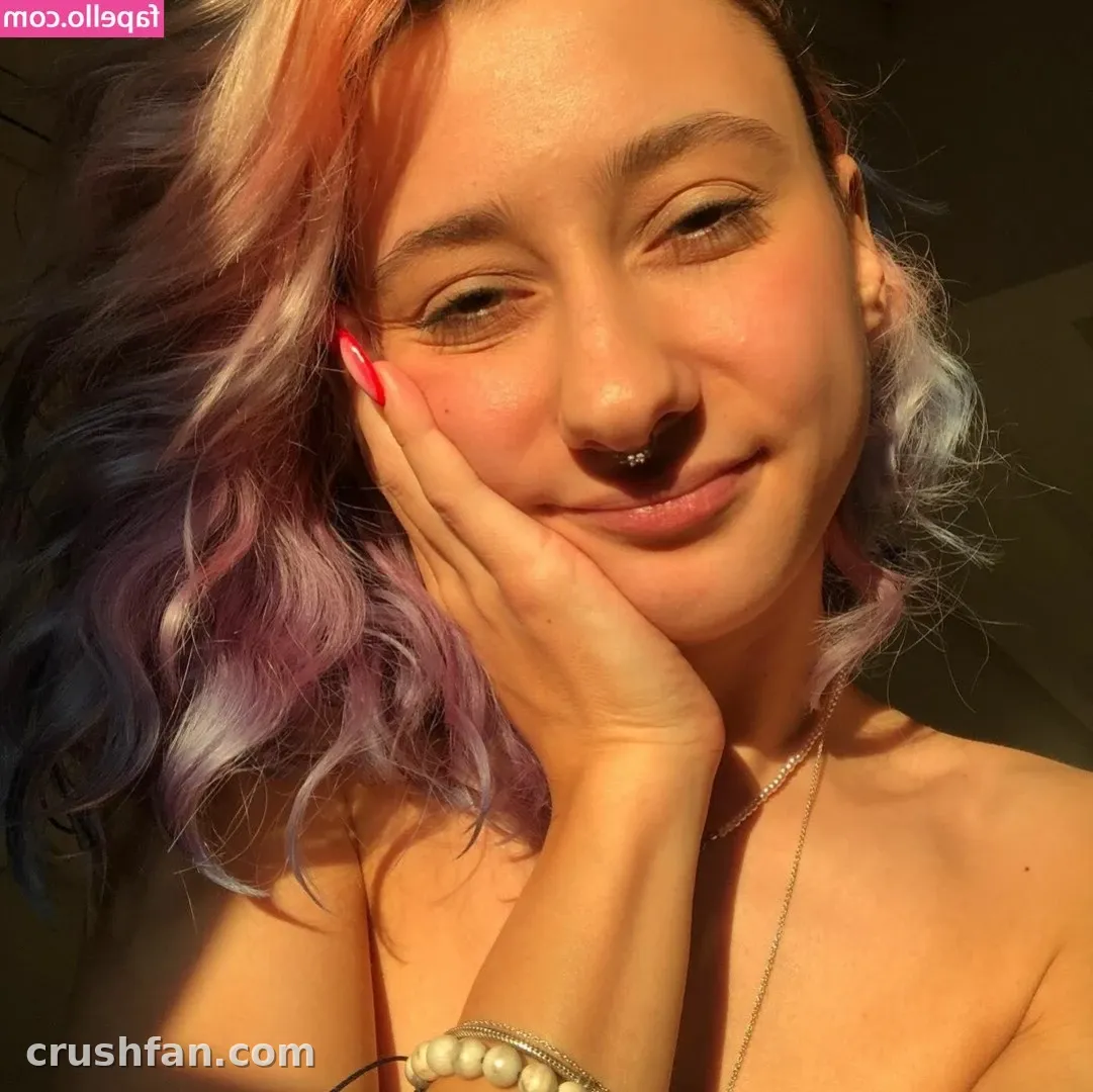 Close-up portrait of 𝐋𝐢𝐥𝐚 with colourful blonde, pink and blue hair, resting her chin on her hand.