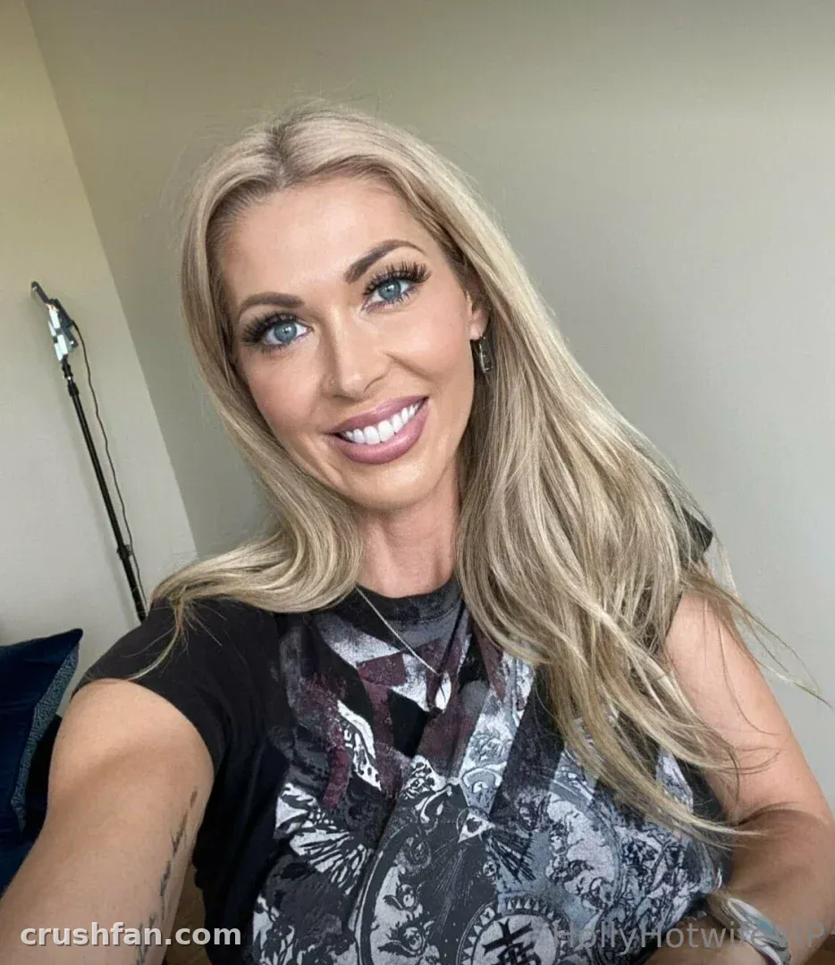 Holly Hotwife smiling in a dark graphic tee during an indoor selfie