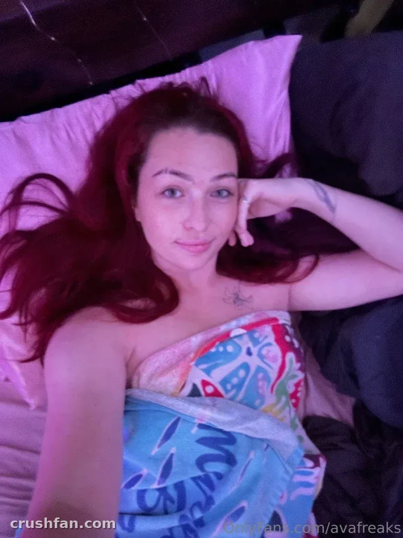 Ava com longos cabelos vermelhos deitada em um travesseiro rosa sob uma luz violeta suave