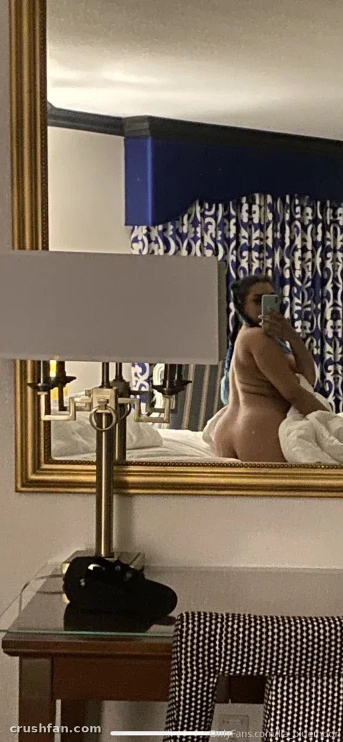 Lia reflected in a gold-framed mirror in a softly lit room with blue curtains