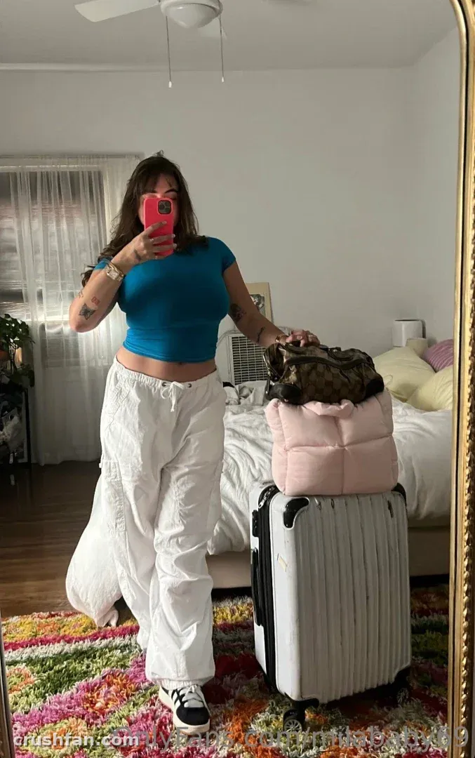 Mila ☆ Baby tomándose una selfie en el espejo en un dormitorio con una maleta y una alfombra colorida.