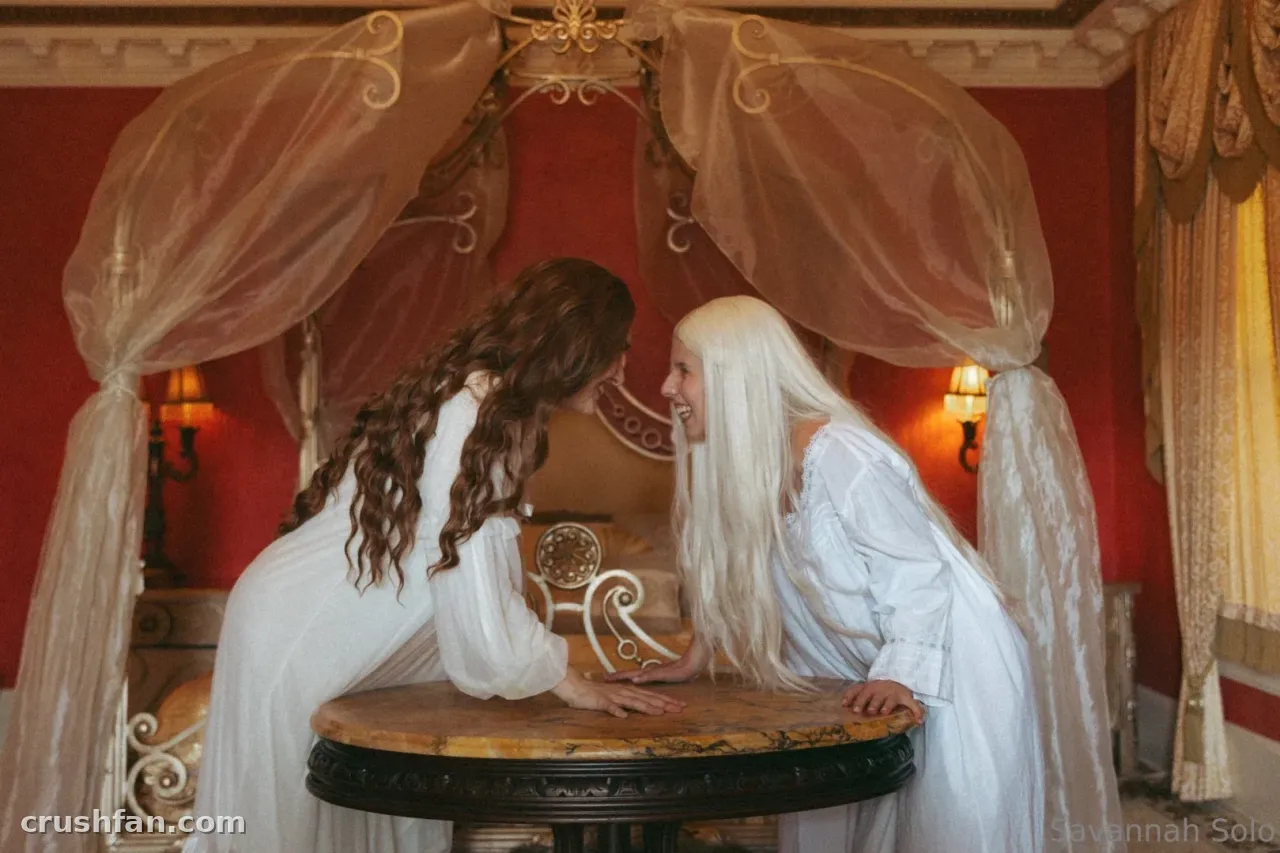 Savannah Solo in a white gown leaning over a table beneath a draped canopy in a red room