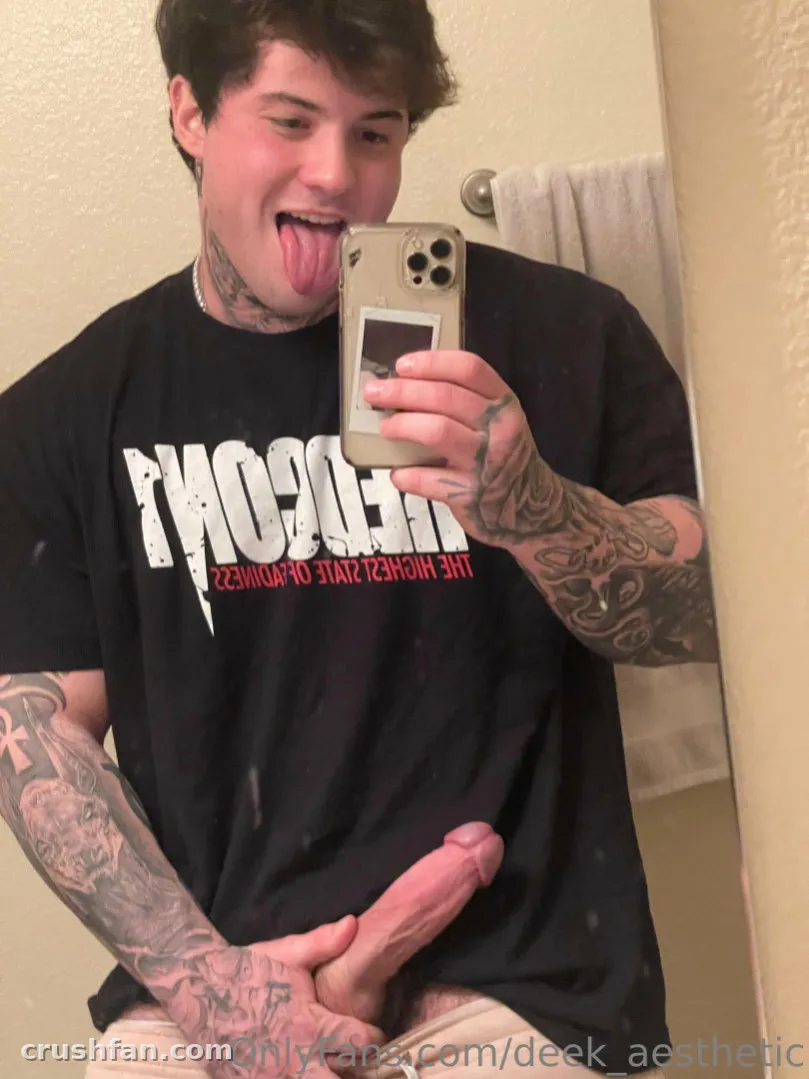 DEEK AESTHETIC taking a mirror selfie in a black graphic tee, showing tattoos.