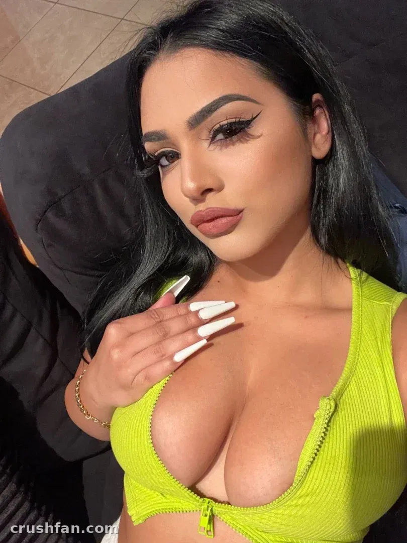 Nadia con un top acanalado verde lima posando para una selfie cercana con uñas largas blancas.