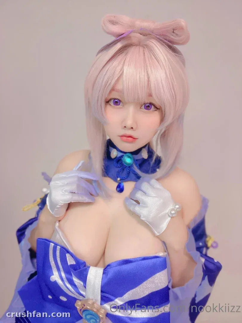 NookkizzCos avec une perruque rose et une tenue de cosplay bleue avec des gants blancs