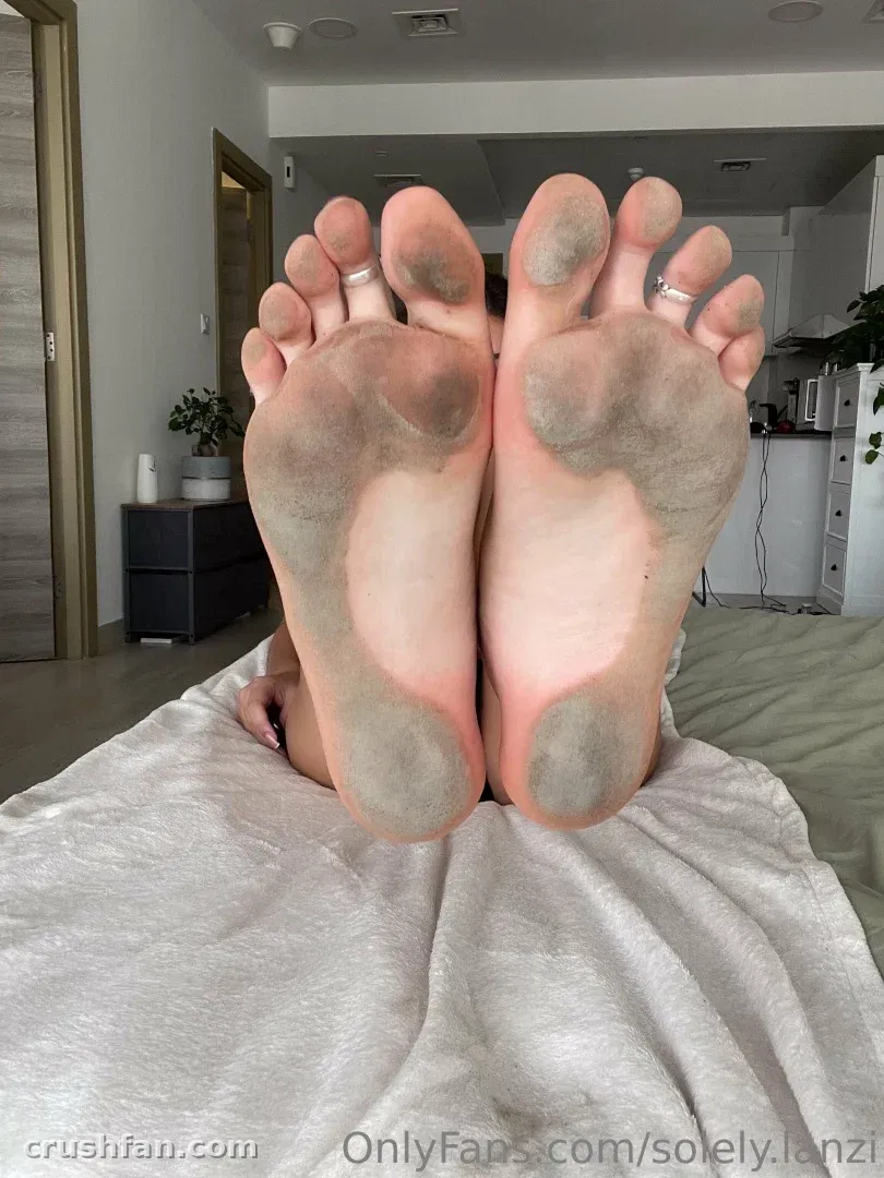 Bare soles of Lanzi's feet facing the camera in a softly lit indoor room