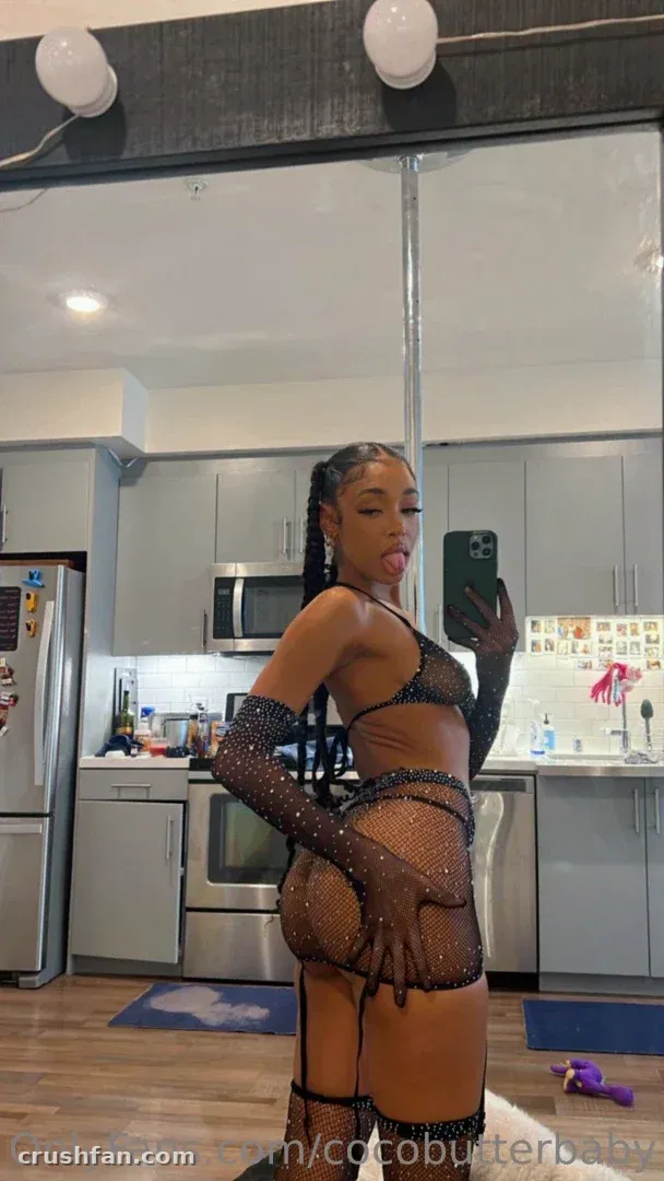 Yara in black rhinestone lingerie and long gloves taking a mirror selfie in a kitchen.