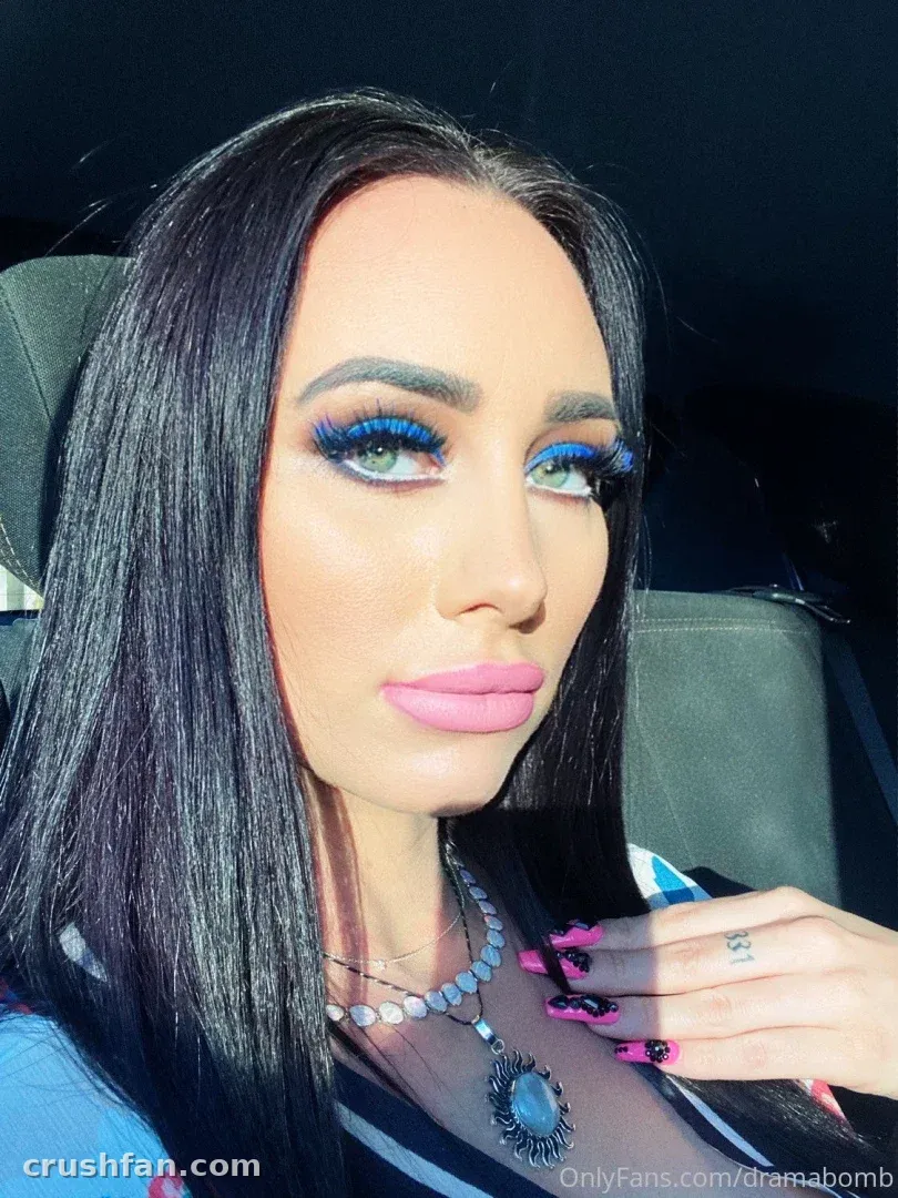 Close-up car selfie of a woman with long dark hair, blue eyeshadow and a beaded pendant necklace