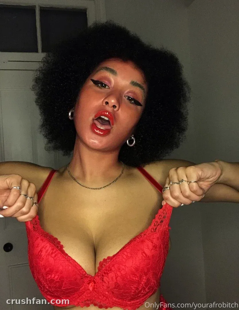 Melissa Ngcobo in a red lace bralette, holding the straps, indoors.