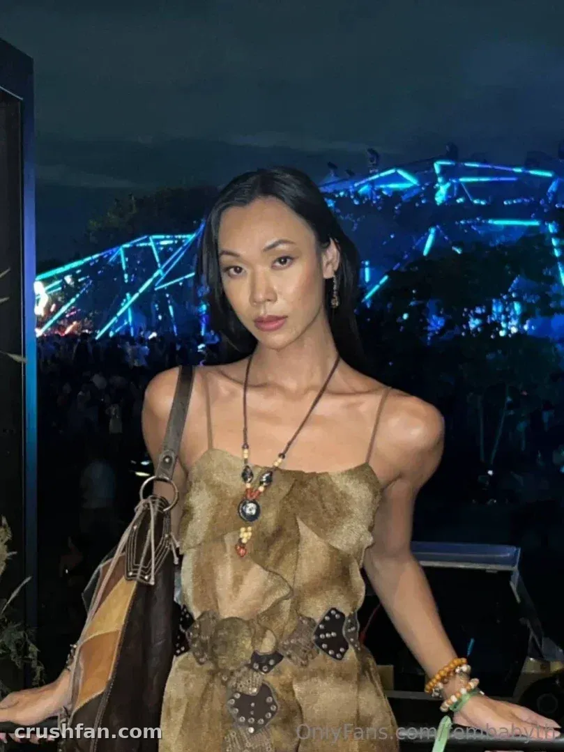Femby com um look marrom texturizado e um colar de contas em um evento noturno com luzes azuis.