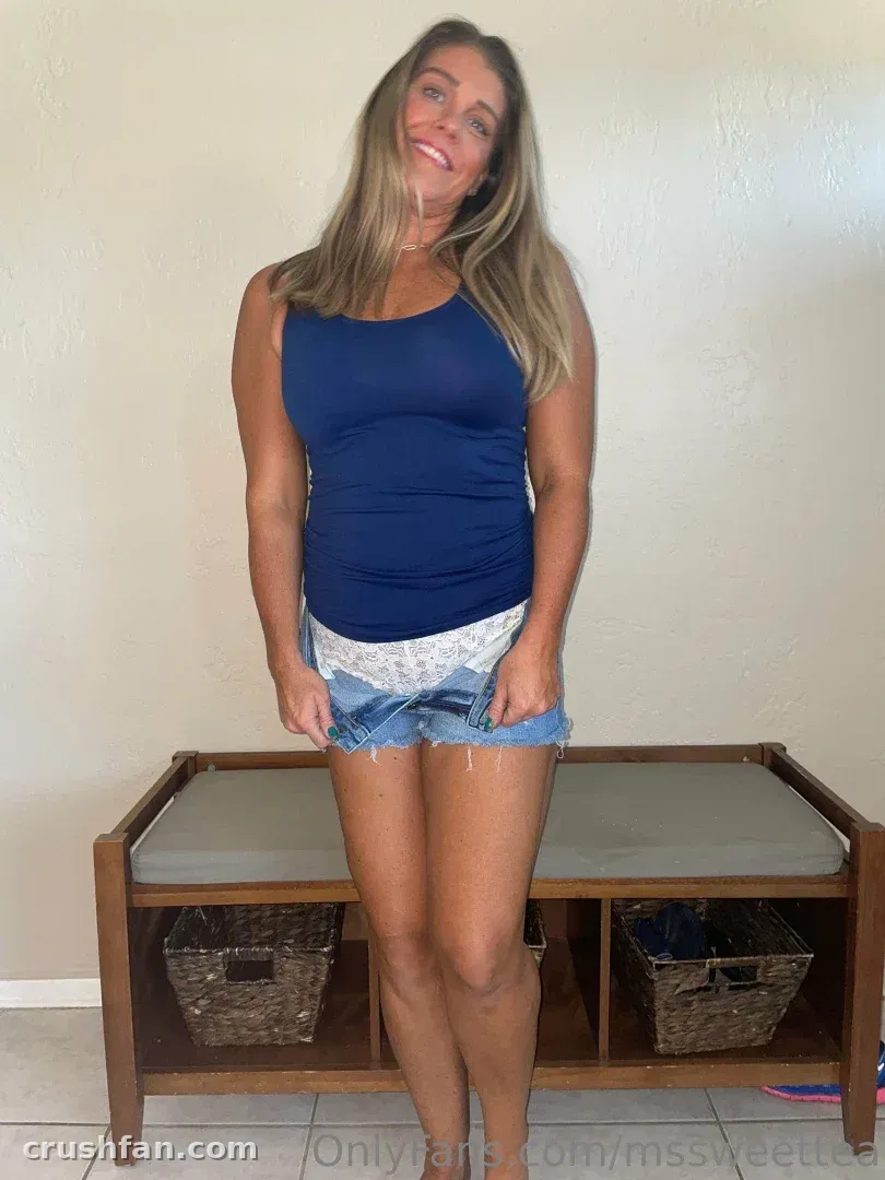 Femme souriante en débardeur bleu marine et short en jean debout devant un banc en bois