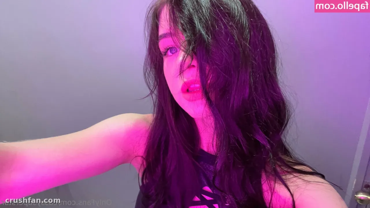 Créatrice aux longs cheveux foncés dans une lumière rose et violette, portant un haut noir sans manches