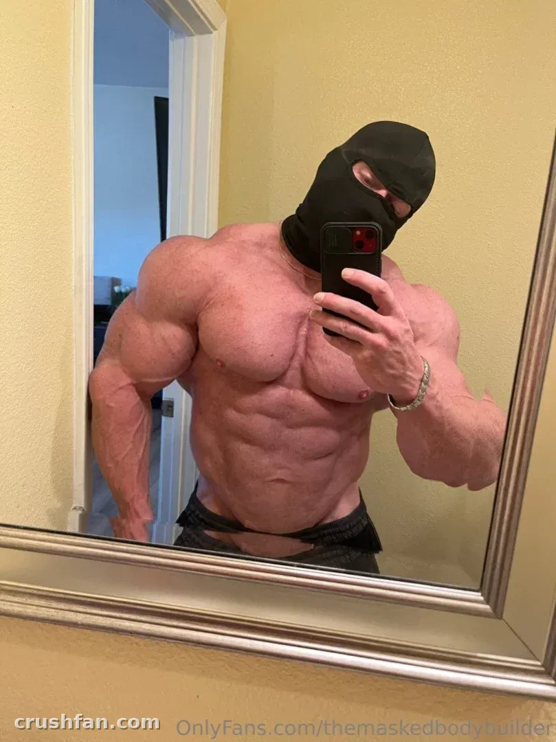 Muscular masked creator taking a mirror selfie in a room with yellow walls