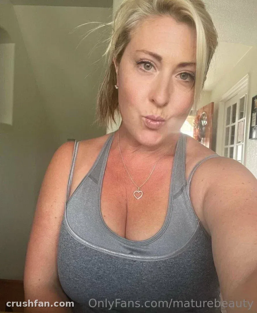 Nita Marie con un top gris y un collar con forma de corazón tomándose una selfie en interiores.