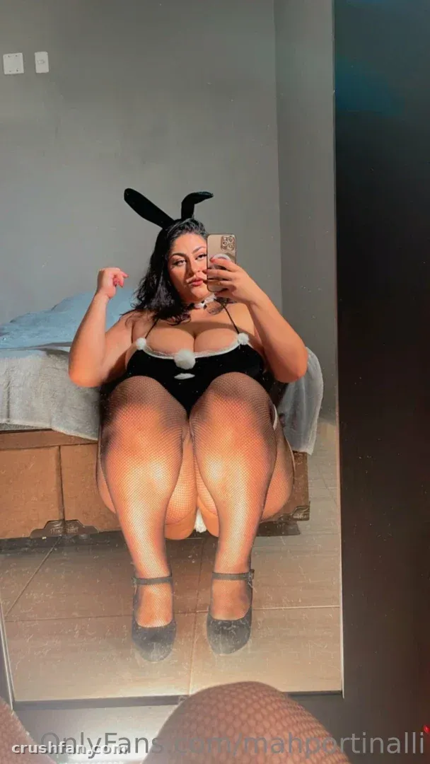 Marcela dans une tenue de lapine noire prenant un selfie dans le miroir tout en étant assise à l'intérieur.
