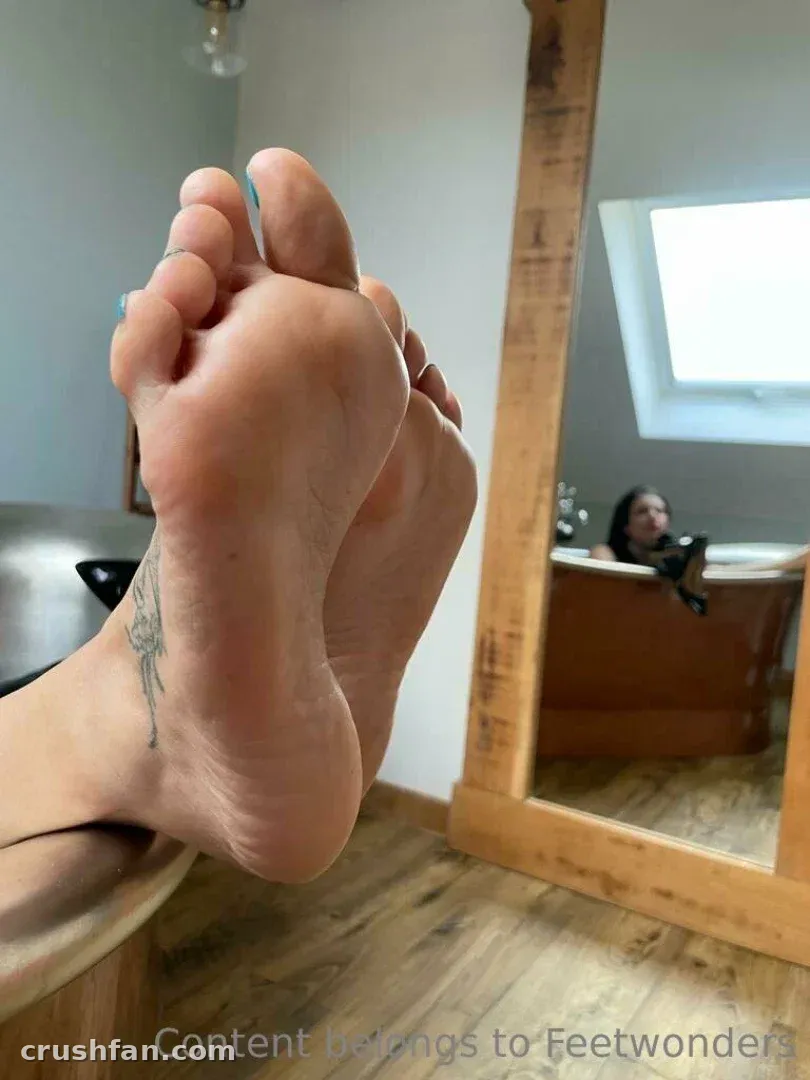 Gros plan sur des pieds nus avec un tatouage à la cheville, reflétés dans un miroir à côté d'une baignoire en bois