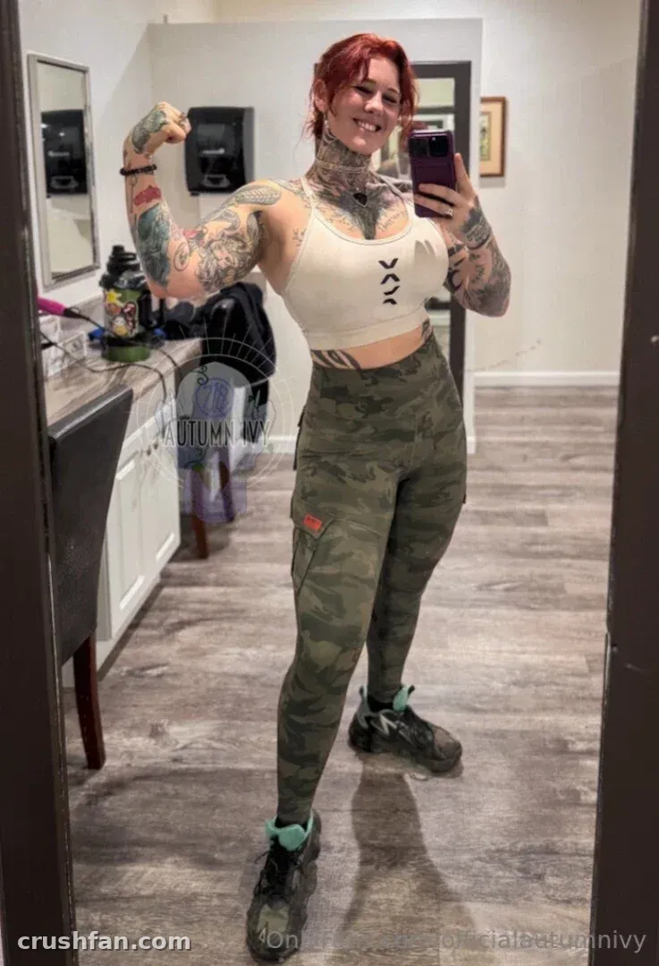 Autumn Ivy in a cropped top and camo leggings taking a mirror selfie while flexing