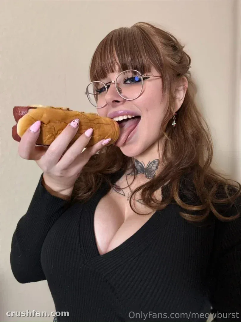 Meowburst holding a hot dog and sticking out her tongue indoors