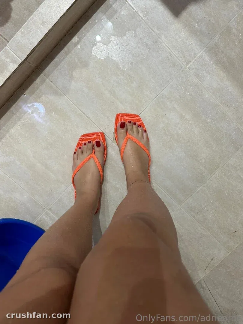 Adripiecitos em pé sobre um piso de ladrilhos usando chinelos laranja vibrantes.