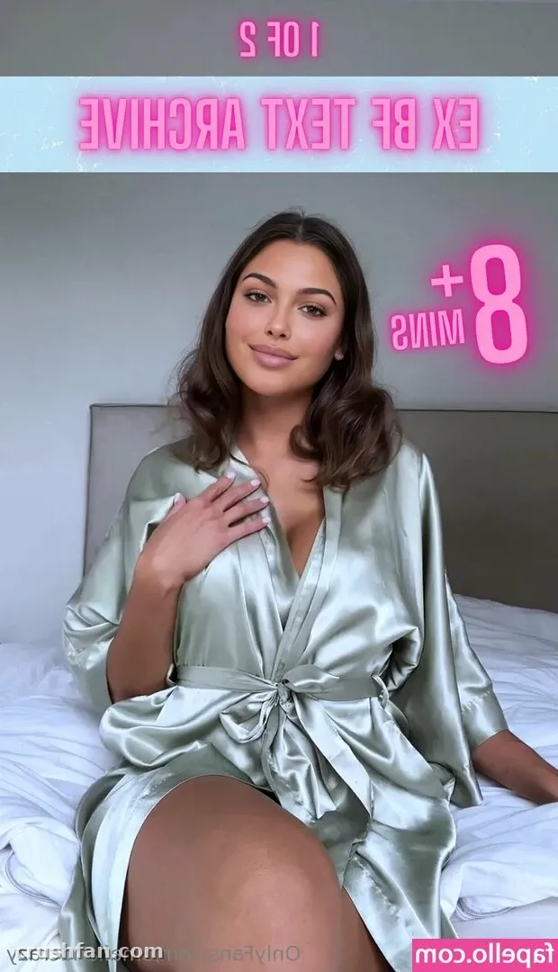 Créatrice en robe de satin vert sauge assise sur un lit blanc avec une tête de lit grise