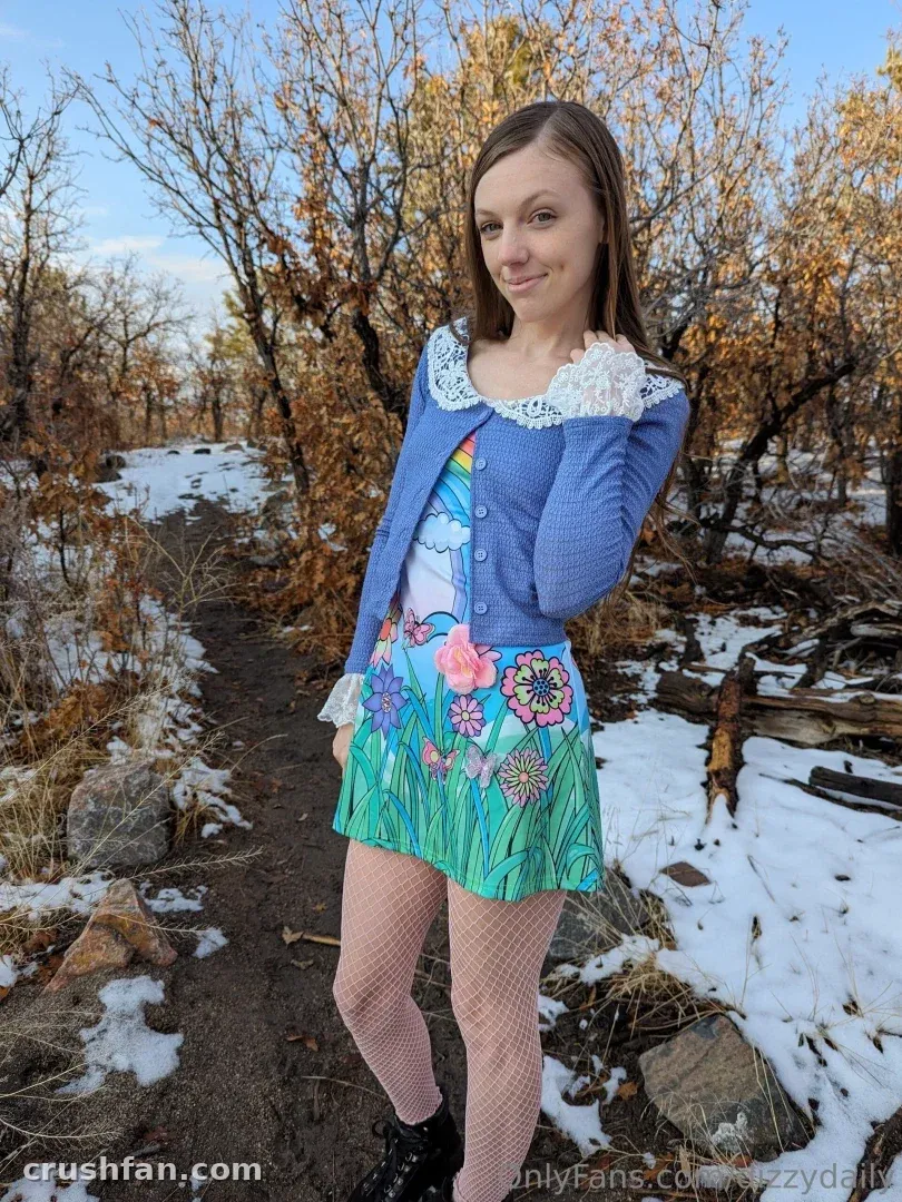 Creator in a blue cardigan and floral dress standing on a snowy woodland trail