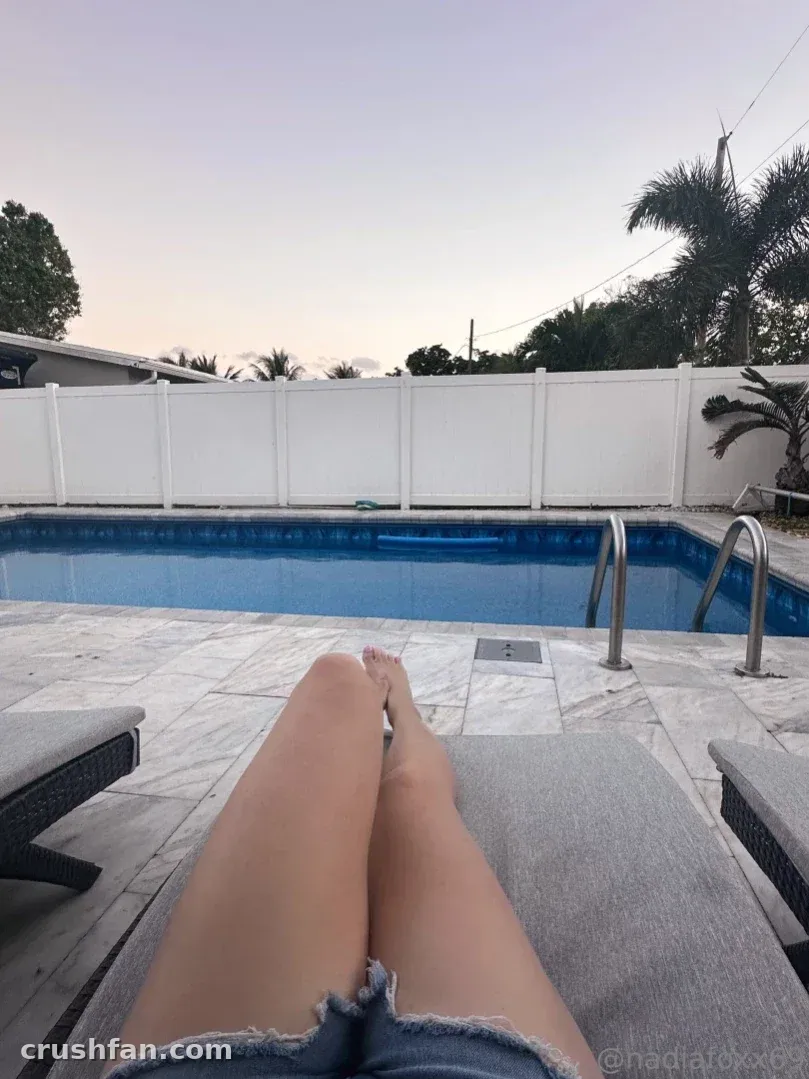 Nadia Foxx reclining by a pool in denim shorts at dusk