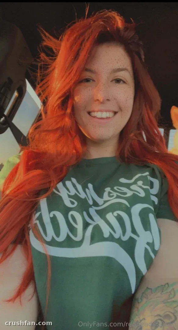 Redhead420 smiling in a green graphic t-shirt with warm lighting