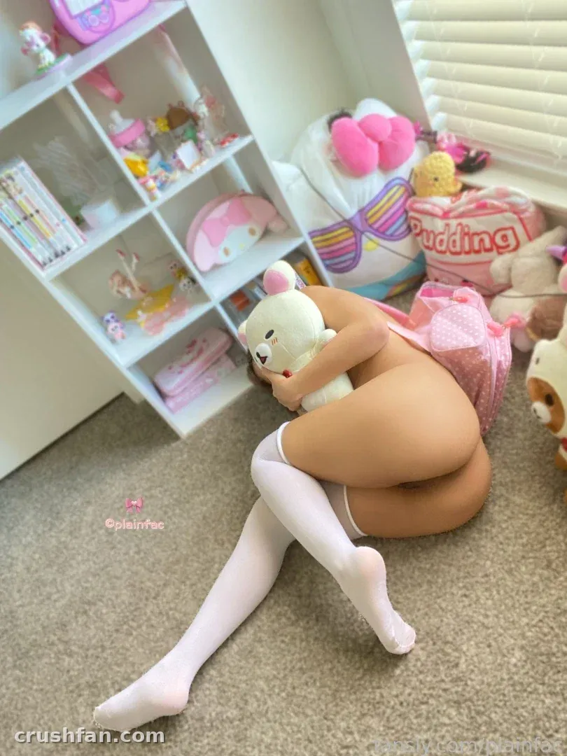 Creator seated on a carpeted floor hugging a white plush bear in a pastel room.