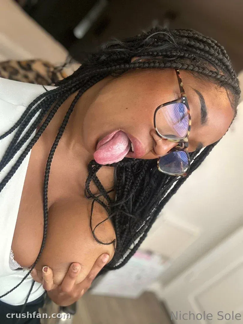 Nichole Sole com cabelo trançado e óculos em um retrato interno próximo