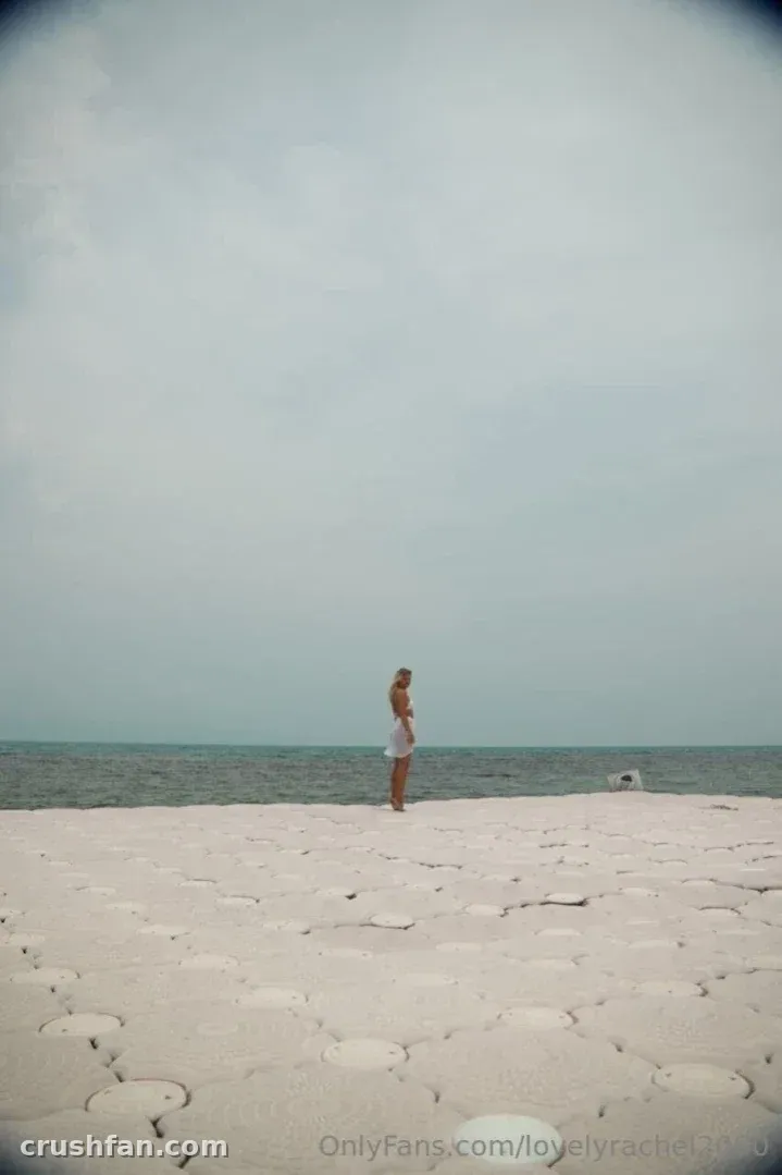 Lovely❤️Rachel steht an einem blassen Sandstrand unter einem weiten grauen Himmel