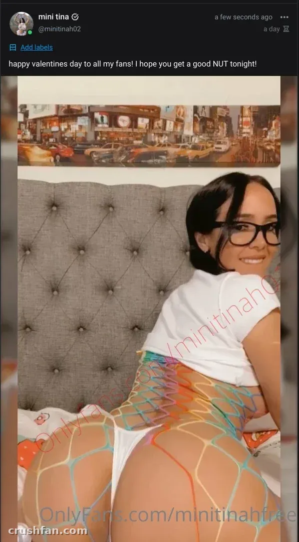 The real Minitinah smiling in a bedroom wearing a white top and fishnet tights.