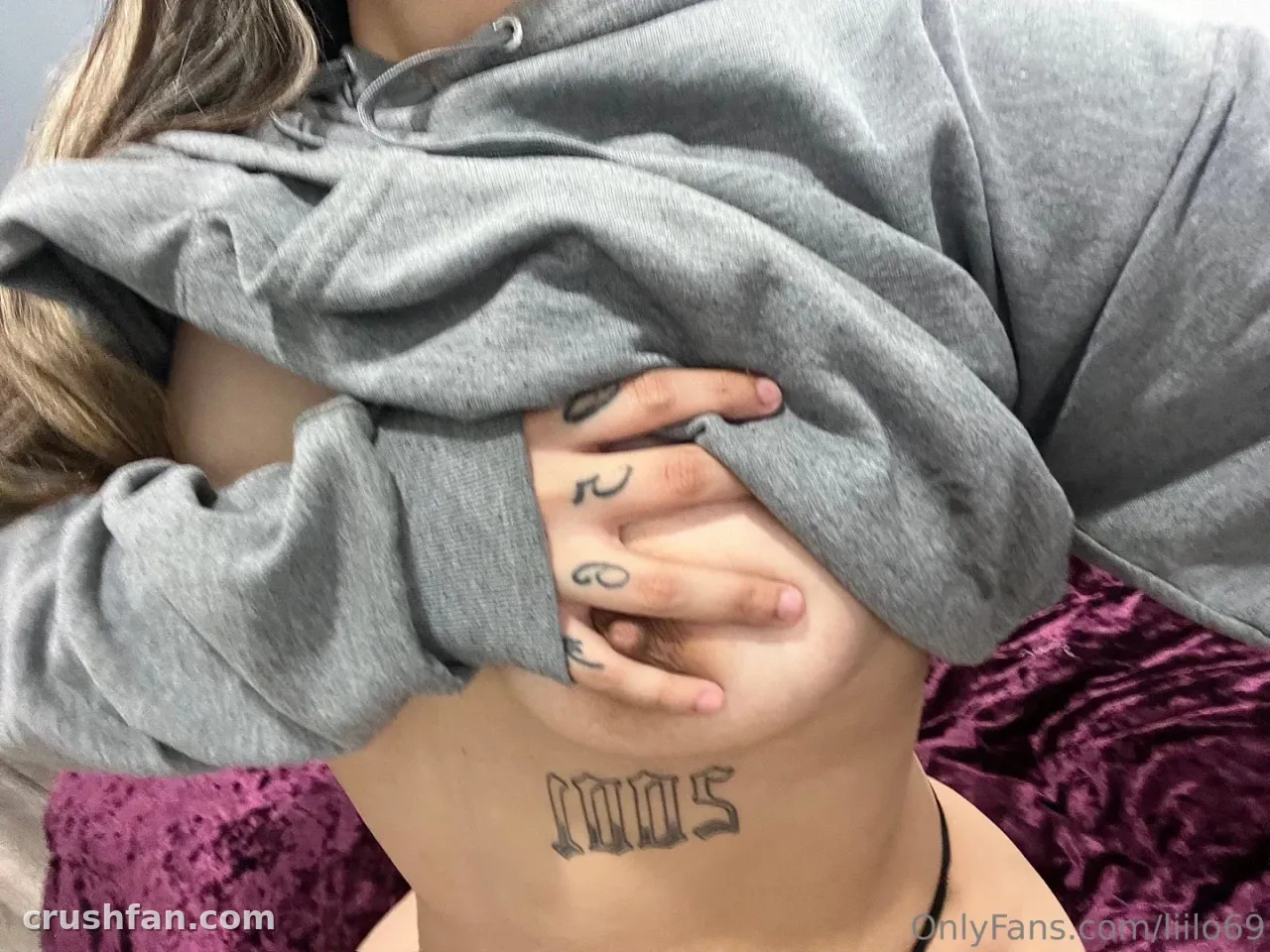 Liilo69 dans un sweat à capuche gris sur un fond violet texturé