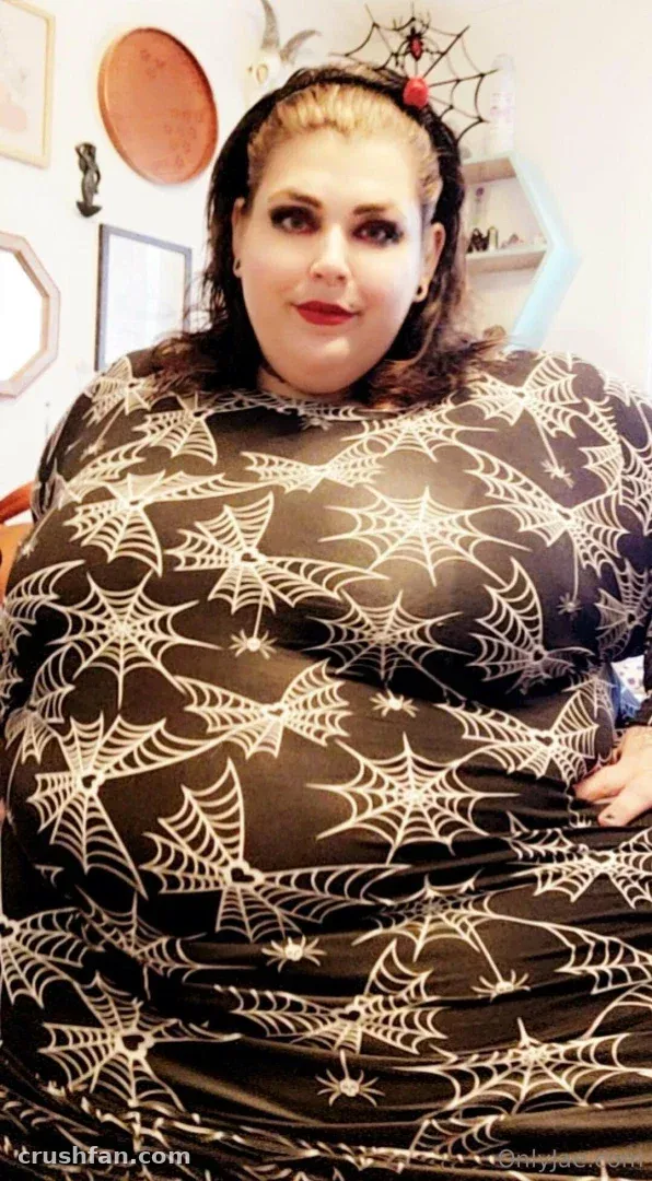Jae Moonbeam wearing a black dress with a white spiderweb pattern and a red-accented headband indoors.