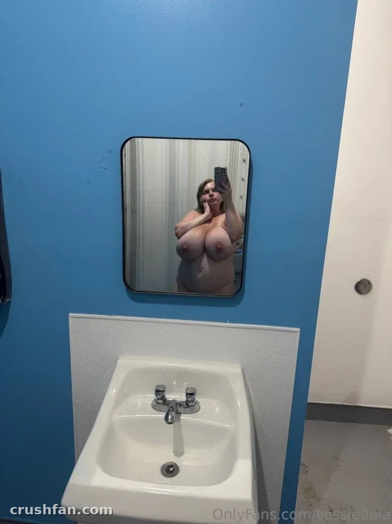 Cassie0pia macht ein Oben-ohne-Spiegel-Selfie in einem blauen Badezimmer mit einem weißen Waschbecken.