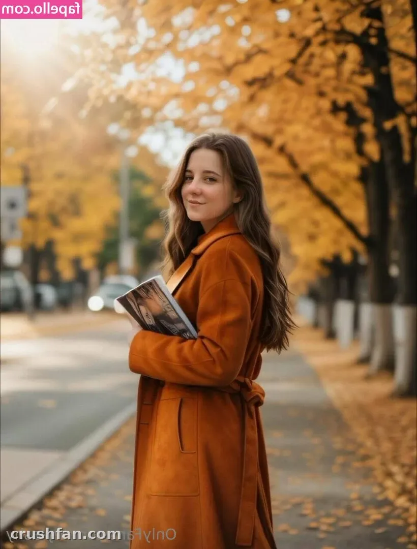 Mulher com um casaco laranja-ferrugem segurando um livro em uma rua de outono coberta de folhas