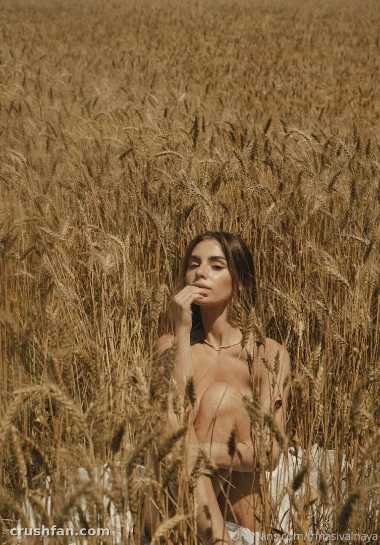 Woman with dark hair seated in a golden wheat field, hand near her chin