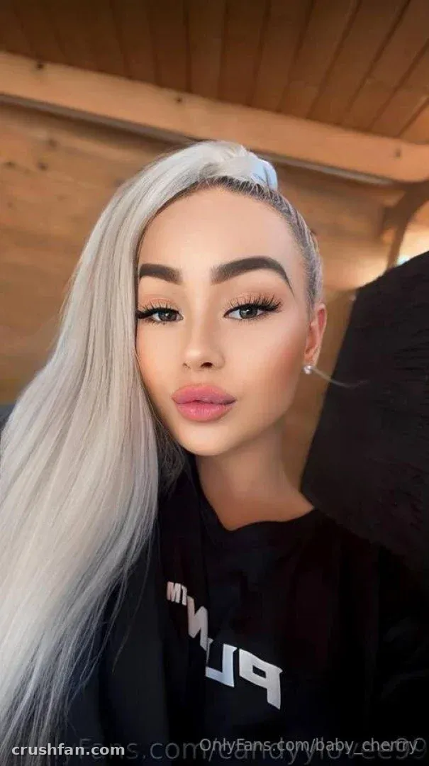 Selfie de cerca de Cherry Blossom con largo cabello plateado y sudadera negra sobre revestimiento de madera