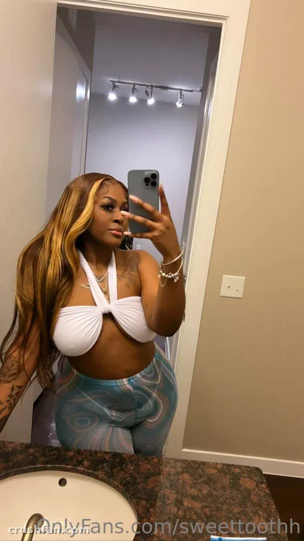 Sweettoothh in a white halter top and swirl leggings taking a mirror selfie in a bathroom.