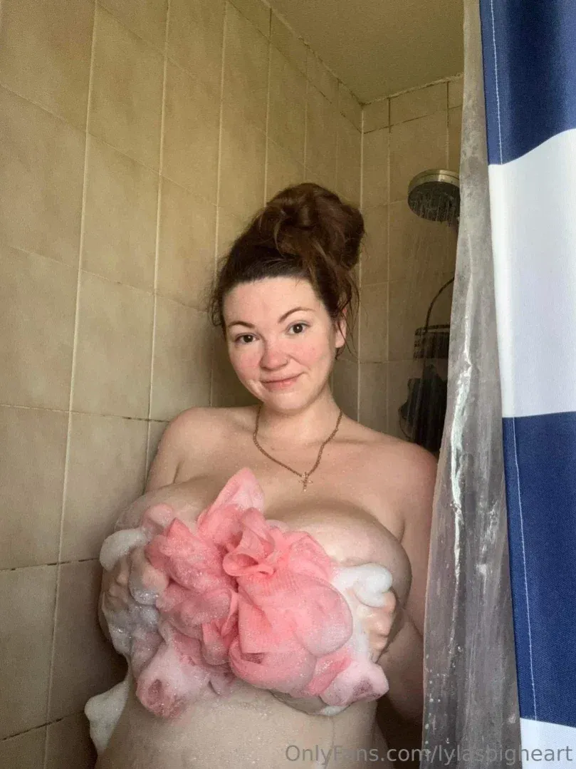 Lyla smiling in a tiled shower holding a pink foamy loofah