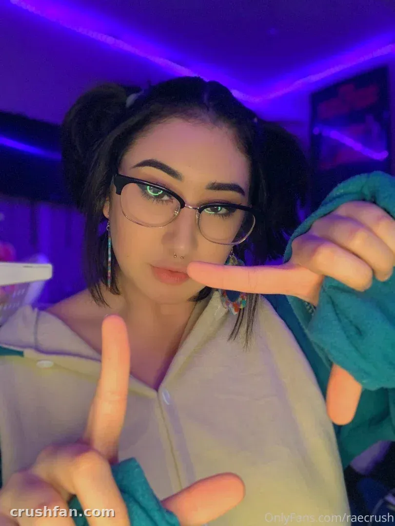 Rae in glasses and a light top with teal sleeves, posing under purple neon light