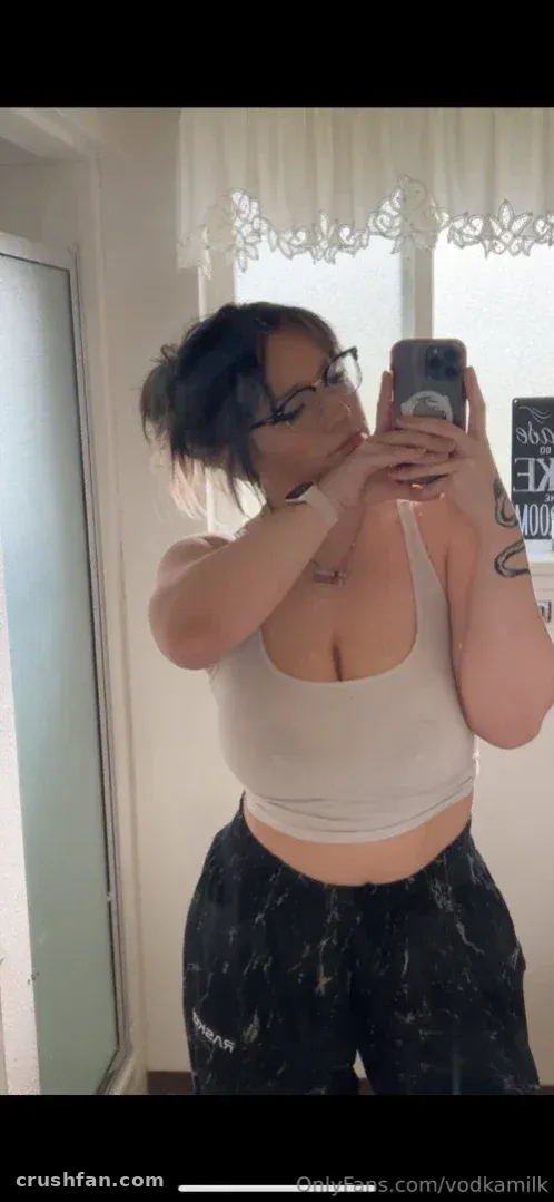 VODKAMILK in a white crop top and dark trousers taking a mirror selfie indoors