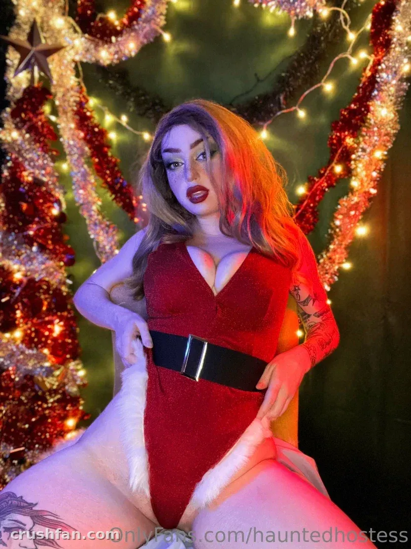 Creator in a red bodysuit and black belt posing among holiday tinsel and warm string lights