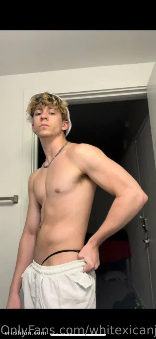 Creator standing indoors in white sweatpants and a chain necklace beside a doorway