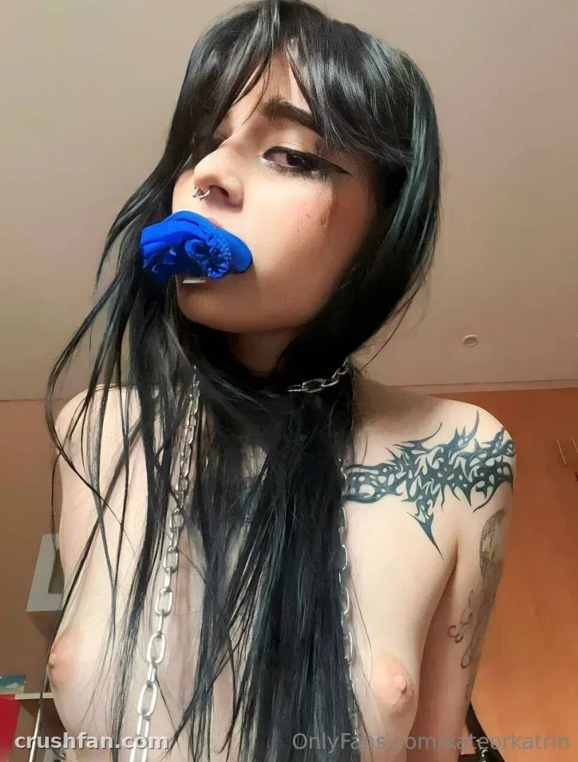 Kate Alyri with dark hair, blue fabric in her mouth and a silver chain, indoor portrait
