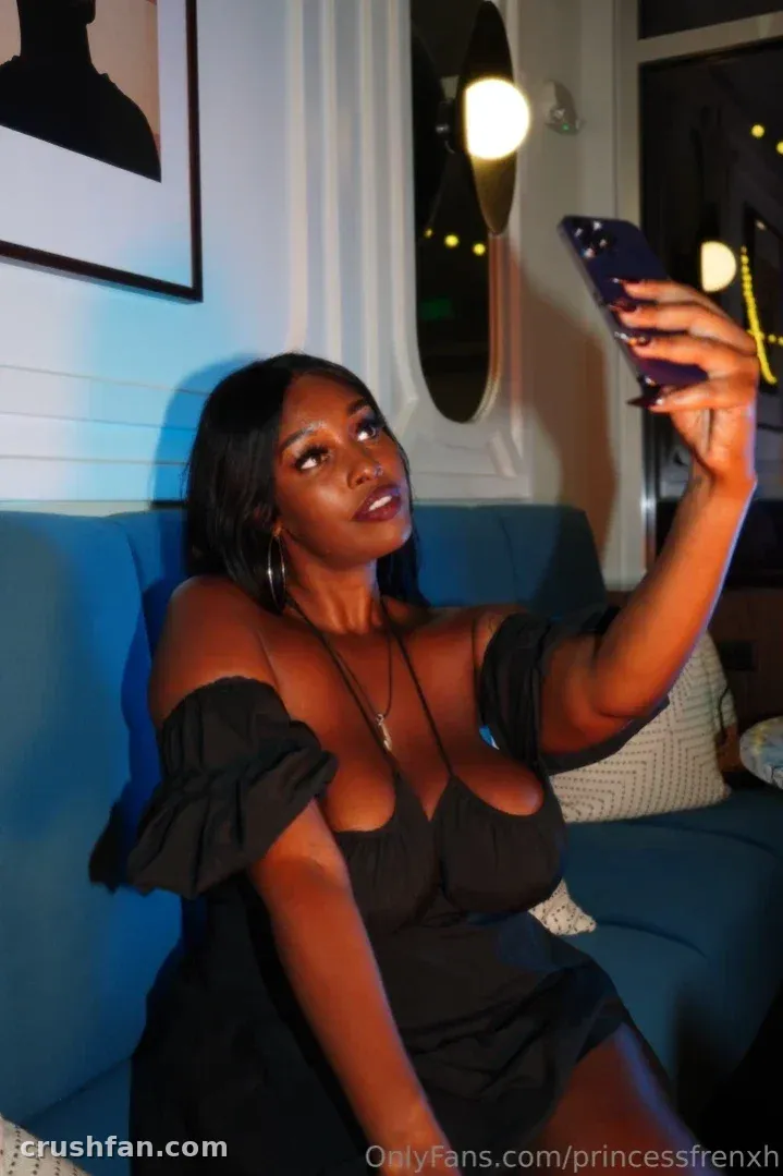 Princess Frenxh in a black off-shoulder dress taking a selfie on a blue sofa indoors