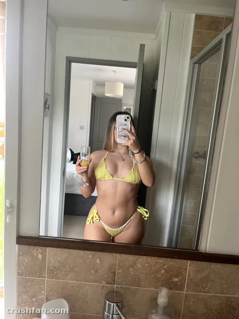 The Katie de biquíni amarelo tirando uma selfie no espelho em um banheiro.